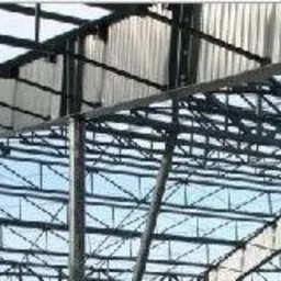 Konstrukcja stalowa dachu hali produkcyjnej widziana od wewnątrz, z logo IMDM.pl po lewej stronie. Widoczne liczne elementy kratownicowe i poszycie dachu.