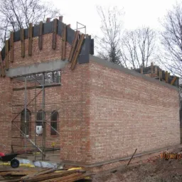 Budowa budynku z czerwonej cegły w trakcie realizacji. Widoczne rusztowania, drewniane elementy konstrukcyjne i częściowo wzniesione mury. Data na zdjęciu: 10/01/2012.