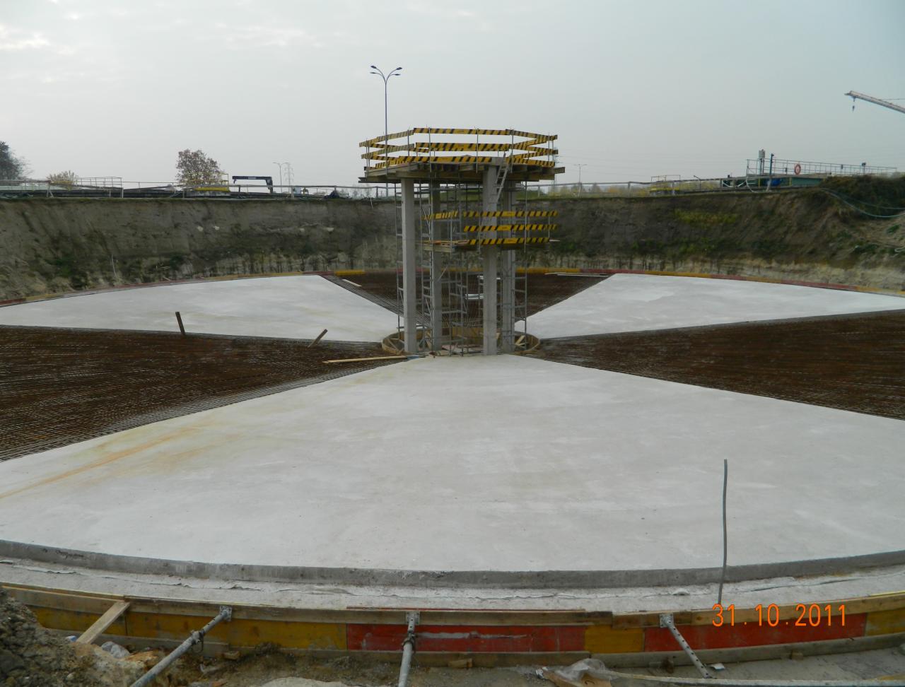 Fundament zbiornika w trakcie budowy: centralna kolumna z platformą, betonowe sektory, zbrojenie. Widoczne szalunki i data 31.10.2011.