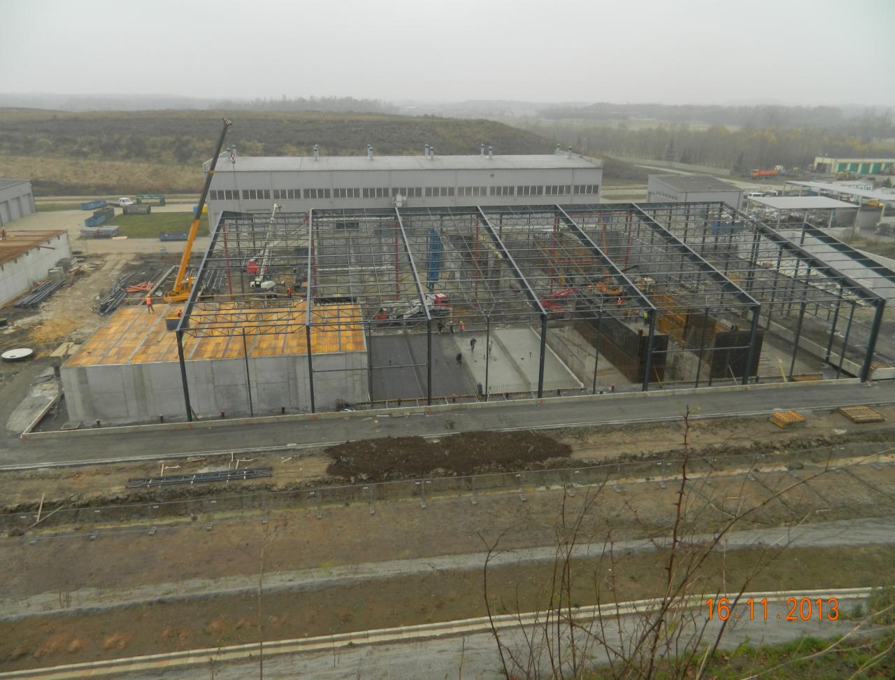 Budowa hali w Tarnowskich Górach: widok z góry na plac budowy z konstrukcją stalową, betonowymi fundamentami i dźwigiem w tle. Etap wznoszenia konstrukcji.