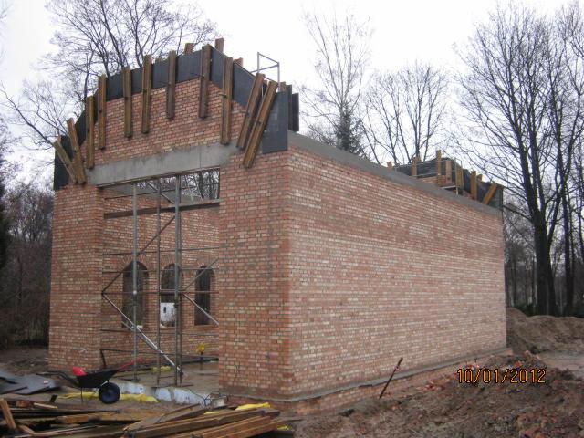 Budowa budynku z czerwonej cegły w trakcie realizacji. Widoczne rusztowania, drewniane elementy konstrukcyjne i częściowo wzniesione mury. Data na zdjęciu: 10/01/2012.