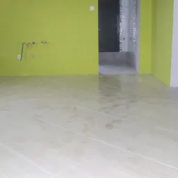 Beżowe płytki podłogowe w nowo wyremontowanym wnętrzu z limonkowymi ścianami. Widoczne przyłącza hydrauliczne i wejście do wykończonej łazienki.