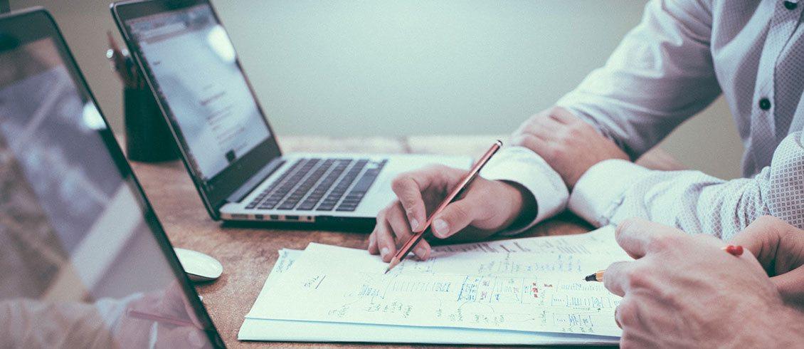 Dwie osoby pracują nad projektem: jedna rysuje schemat na papierze, druga sprawdza dane na laptopie.