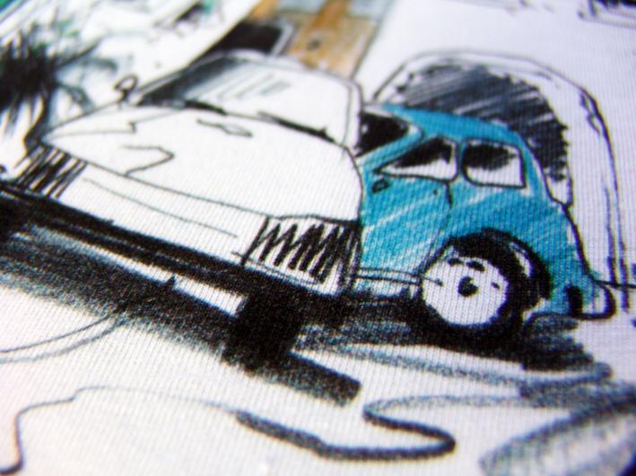 Szczegółowe zbliżenie na białą koszulkę z nadrukiem przedstawiającym stylizowane, ręcznie rysowane samochody w kolorach białym, czarnym i niebieskim.