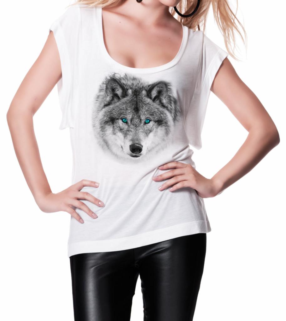 Kobieta w białej koszulce z nadrukiem głowy wilka o błękitnych oczach, pozująca na białym tle w czarnych, skórzanych spodniach.