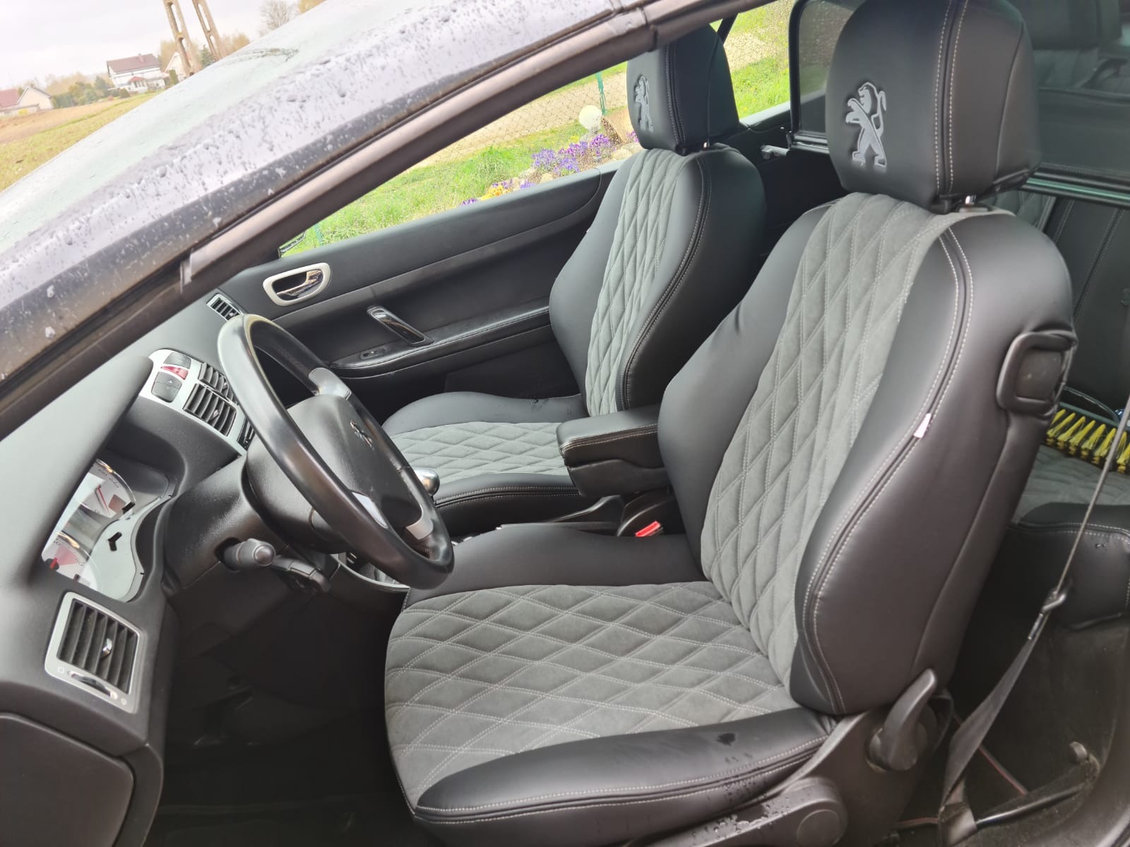 Wnętrze samochodu z nową, pikowaną szarą tapicerką foteli z logo producenta na zagłówkach, widok z perspektywy kierowcy.