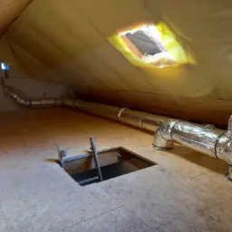 Instalacja wentylacyjna z rurami spiro w izolowanym poddaszu, widoczny właz z drabinką i ocieplenie dachu folią.