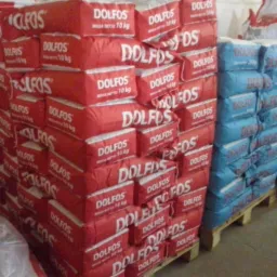 Stos czerwonych worków z napisem DOLFOS (masa netto 10 kg) na paletach, obok niebieskie worki. Magazyn z zapasami.