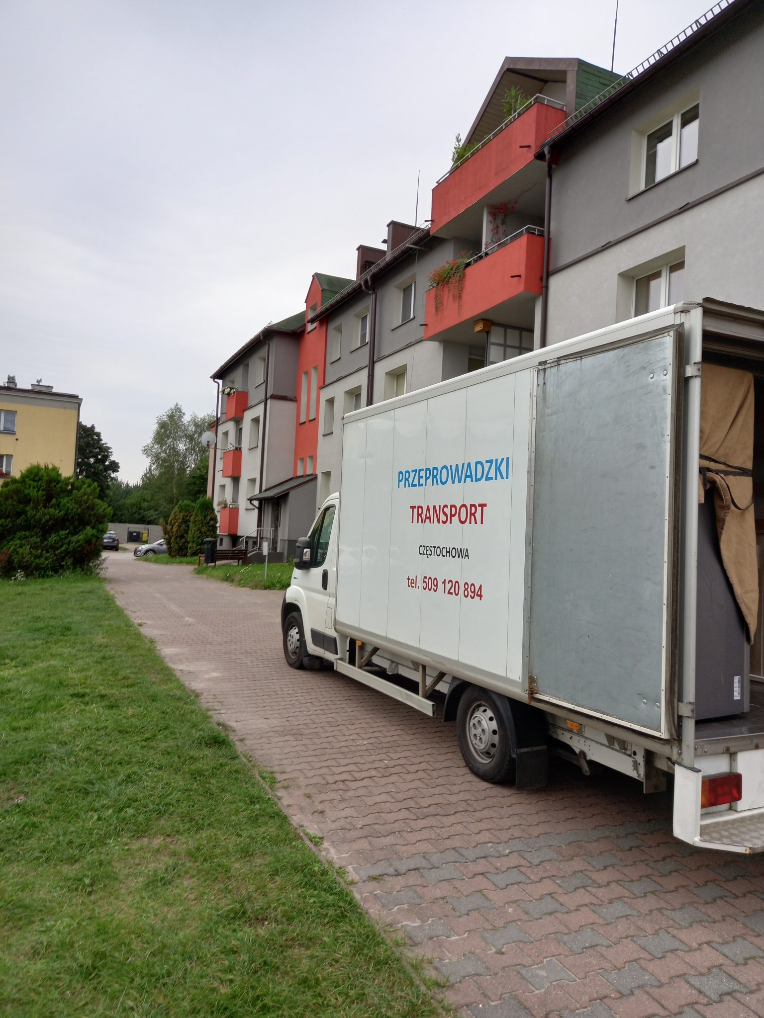 Ciężarówka z otwartymi drzwiami, z napisem 'Przeprowadzki Transport Częstochowa' zaparkowana na chodniku przed blokiem mieszkalnym.