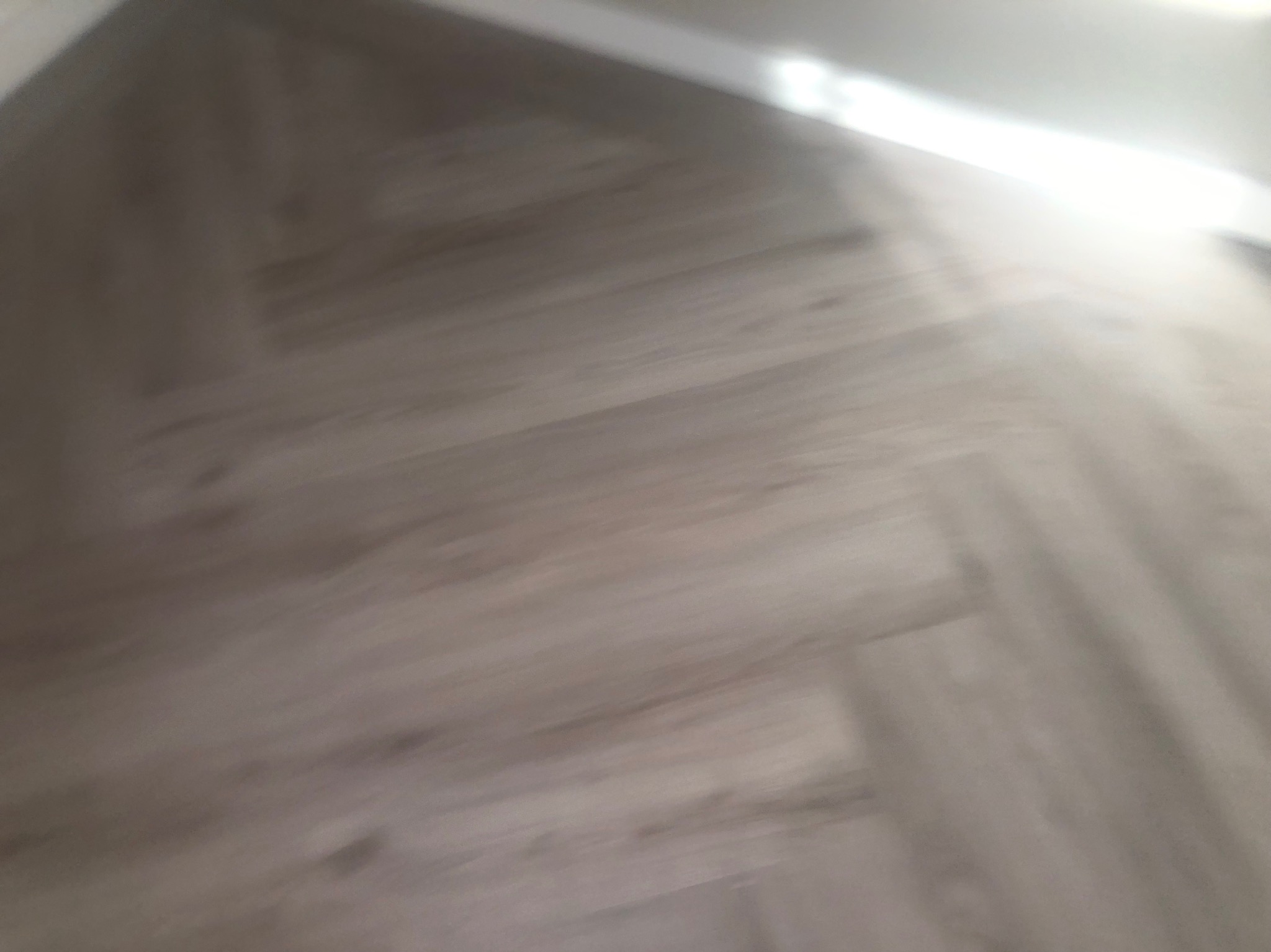 Ułożona pod kątem podłoga panelowa w odcieniach szarości przy białej listwie przypodłogowej, widoczna z góry z lekkim rozmyciem ruchu.