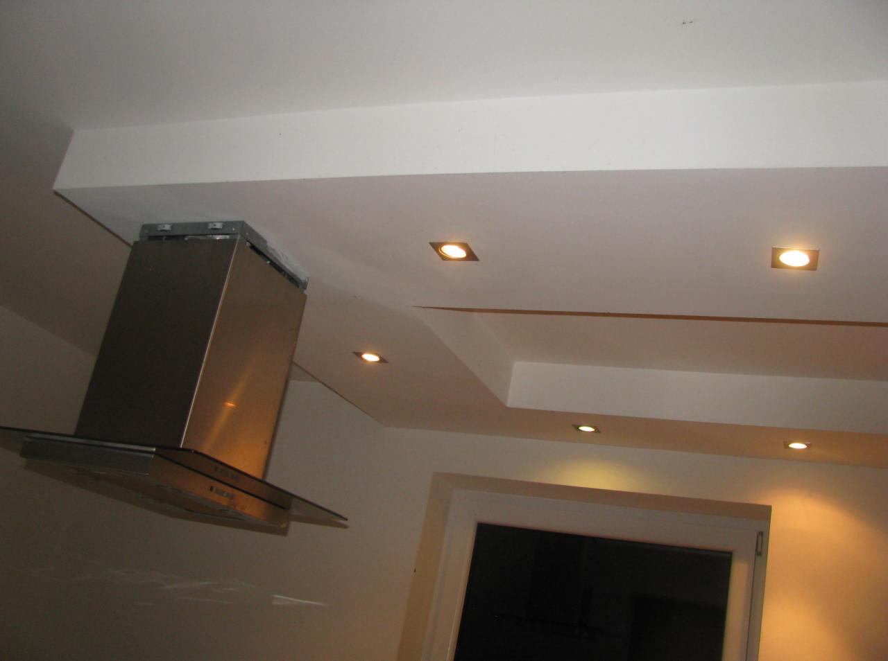 Nowoczesna kuchnia: srebrny okap z szklanym daszkiem zamontowany pod zabudową sufitową z oświetleniem punktowym. Widok na okno.