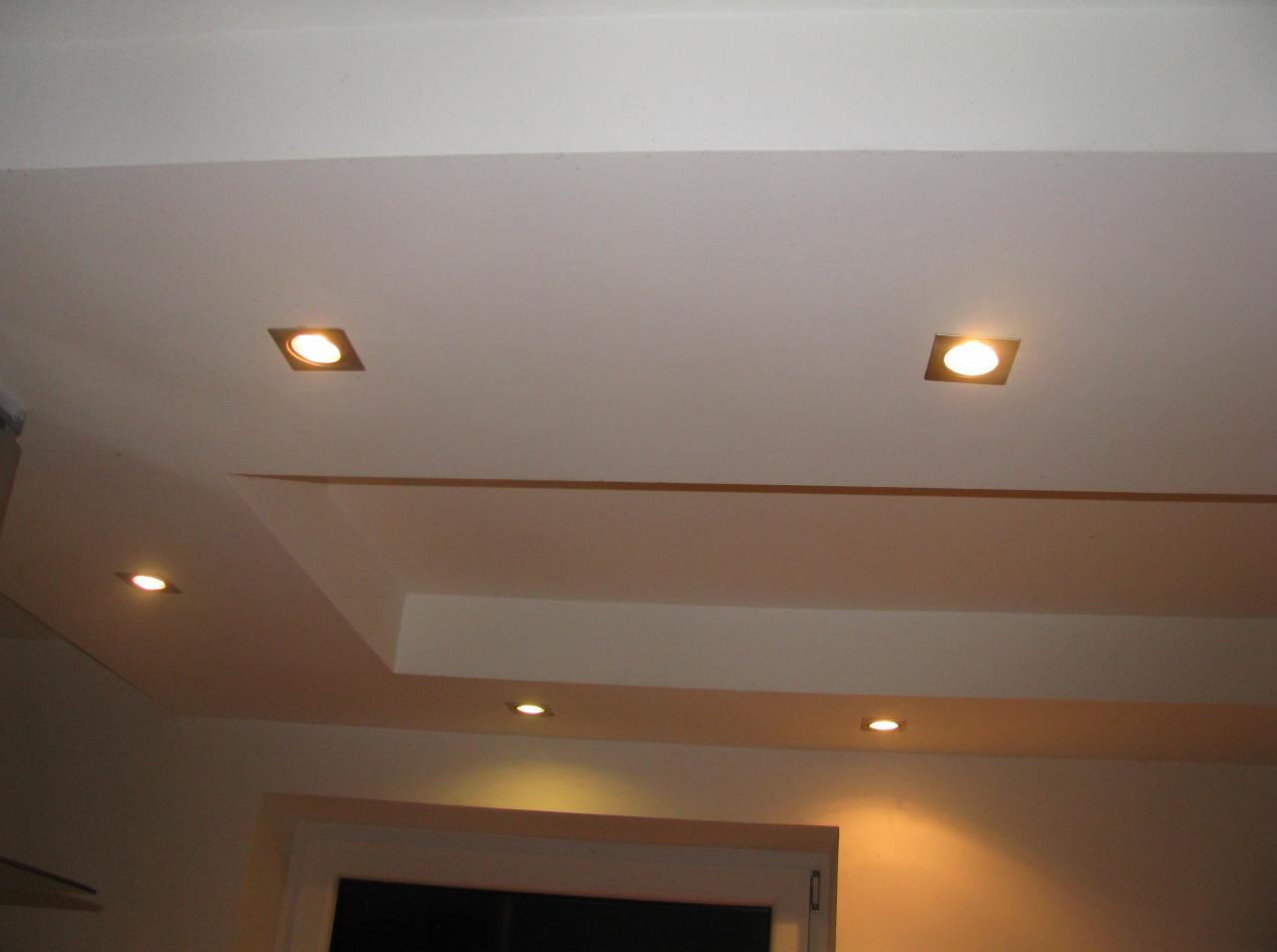 Oświetlenie sufitowe z kwadratowymi lampami punktowymi, biały sufit podwieszany z dekoracyjnymi wgłębieniami, ciepłe światło.