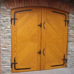 Rustykalne, dwuskrzydłowe drzwi z jasnego drewna, zdobione kutymi zawiasami i klamkami, osadzone w kamienno-ceglanym murze. Widoczne elementy konstrukcji drewnianej.