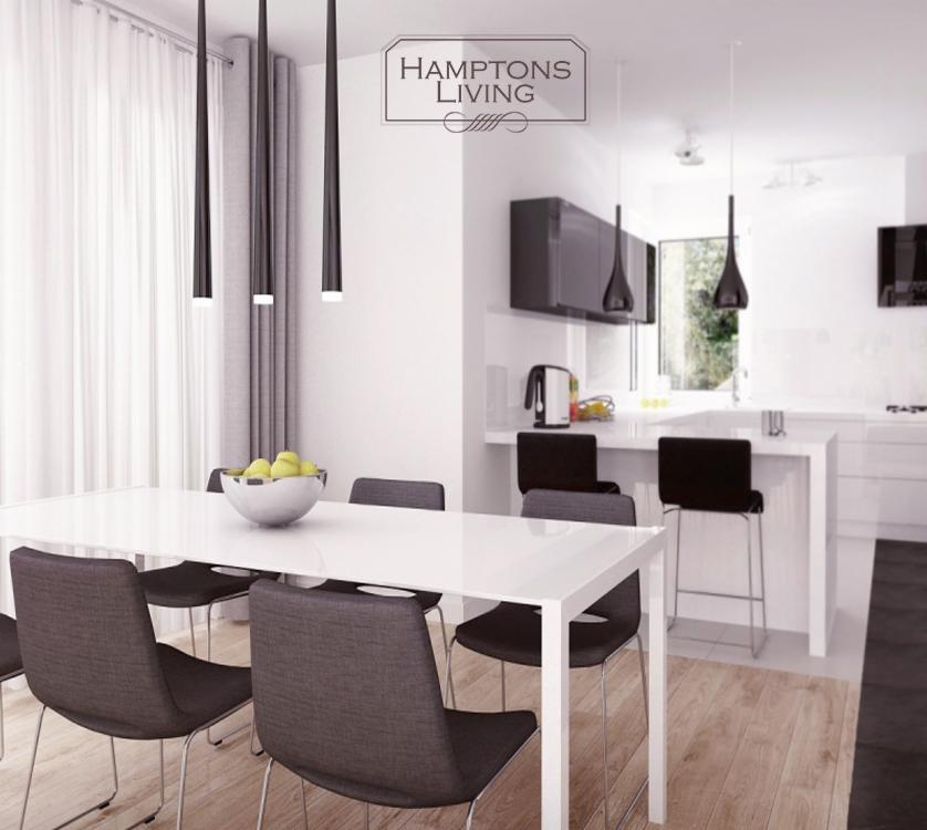 Nowoczesna, jasna jadalnia z białą, błyszczącą kuchnią w tle. Minimalistyczne, czarne lampy wiszące nad stołem. Na stole misa z owocami. Parkiet na podłodze.