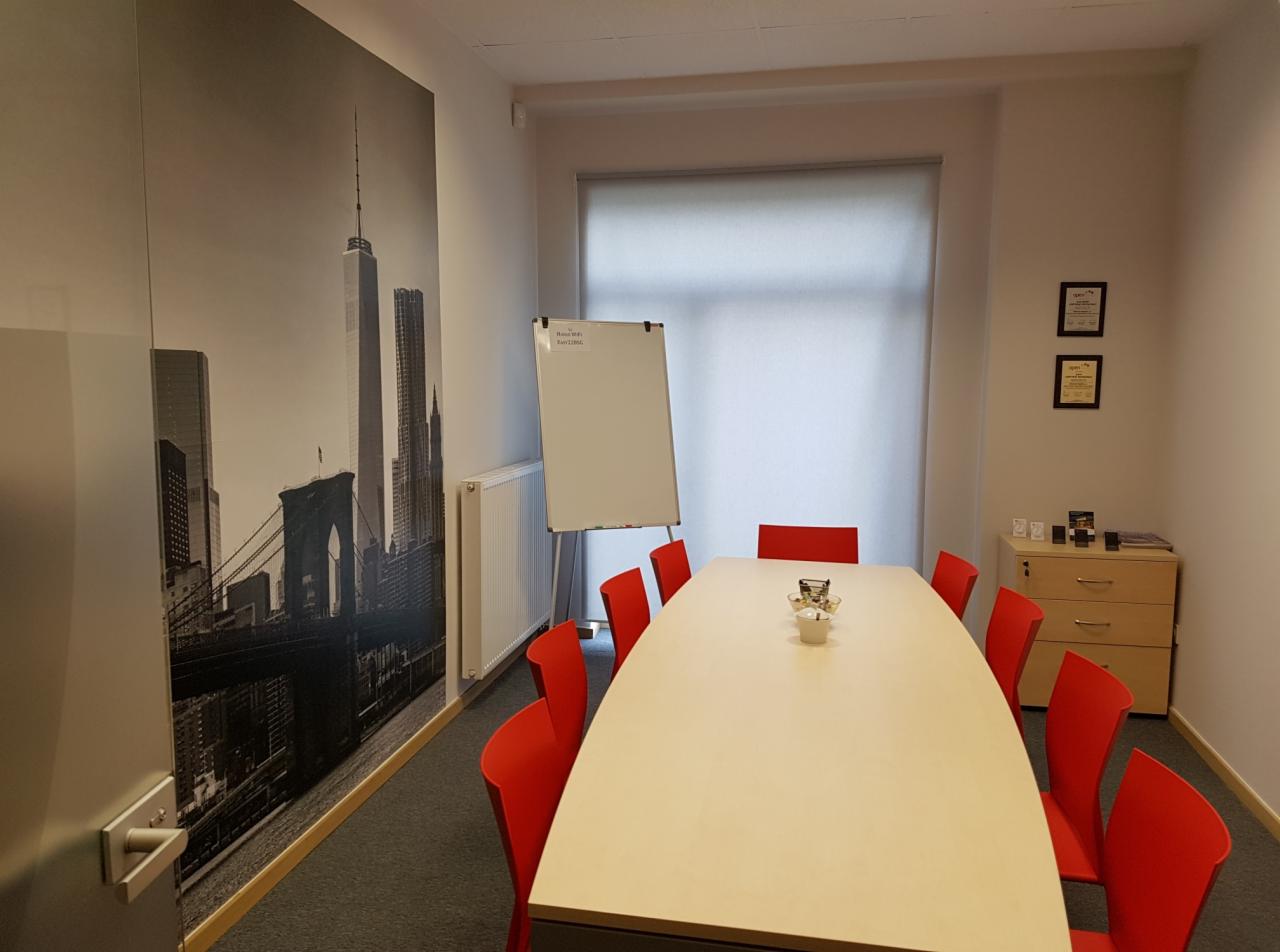 Sala konferencyjna z dużym stołem, czerwonymi krzesłami i fototapetą z widokiem na Nowy Jork.