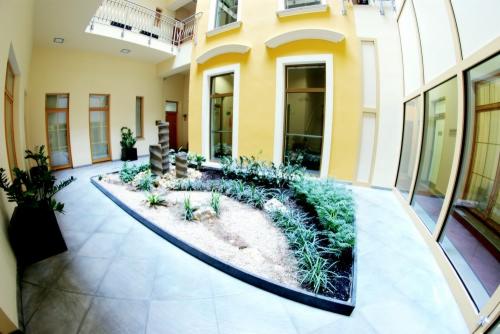 Atrium budynku z centralnym ogrodem z roślinami i rzeźbą, żółte ściany, duże okna, biała podłoga. Widok z perspektywy rybiego oka.