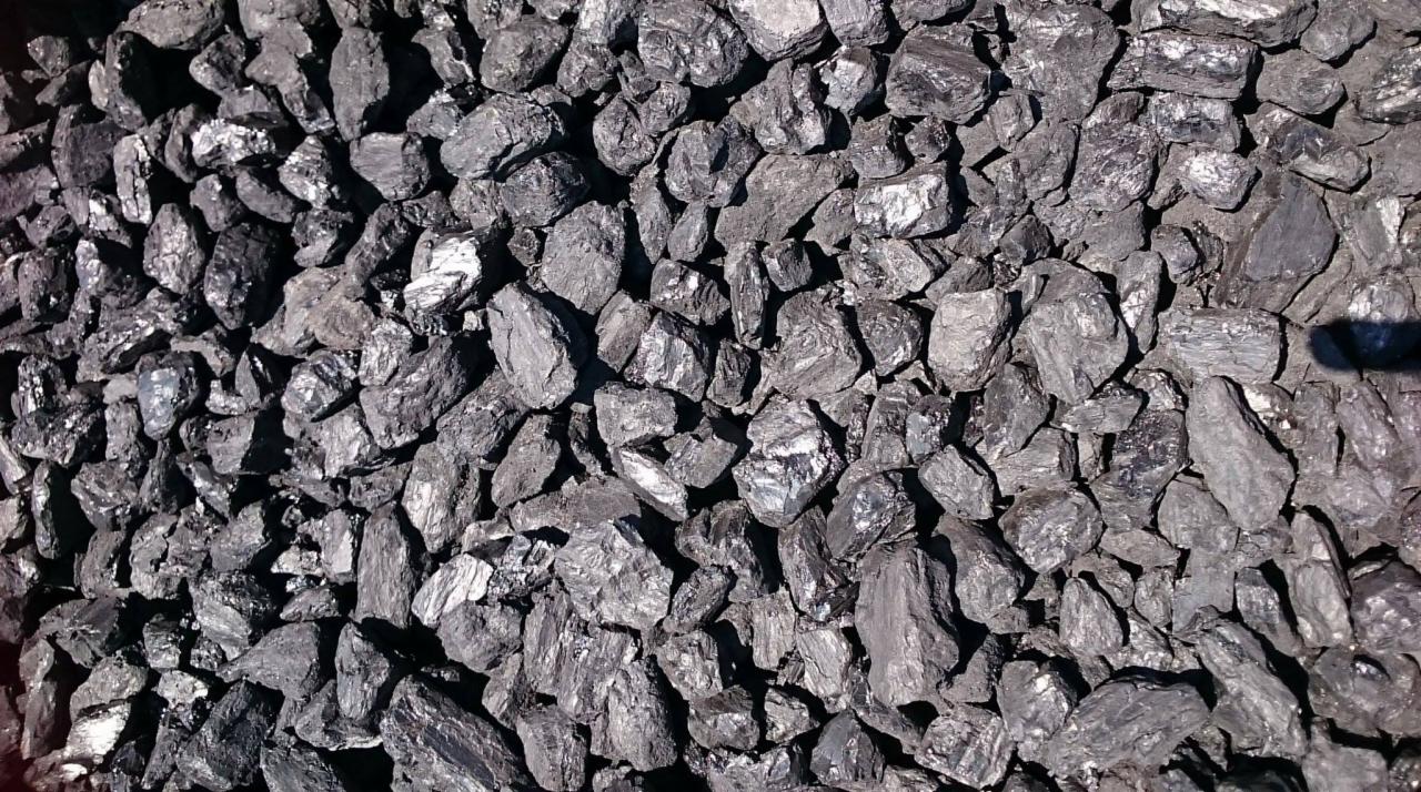 Kupa antracytu o nieregularnych kształtach, oświetlona z góry, z widocznymi refleksami światła na powierzchni bryłek.