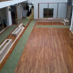 Wnętrze z drewnianą podłogą, zielonym dywanem i elementami dekoracyjnymi. Widok z góry, ukazujący przestronność i unikalny design pomieszczenia.