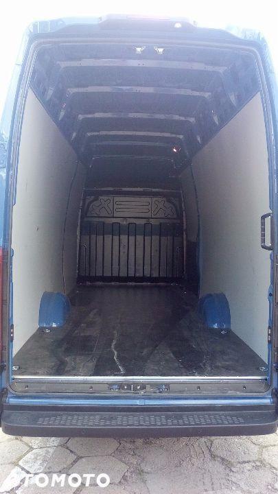 Wnętrze pustej, niebieskiej furgonetki transportowej z otwartymi tylnymi drzwiami, widok z zewnątrz na przestrzeń ładunkową z szarą podłogą i białymi ścianami bocznymi.