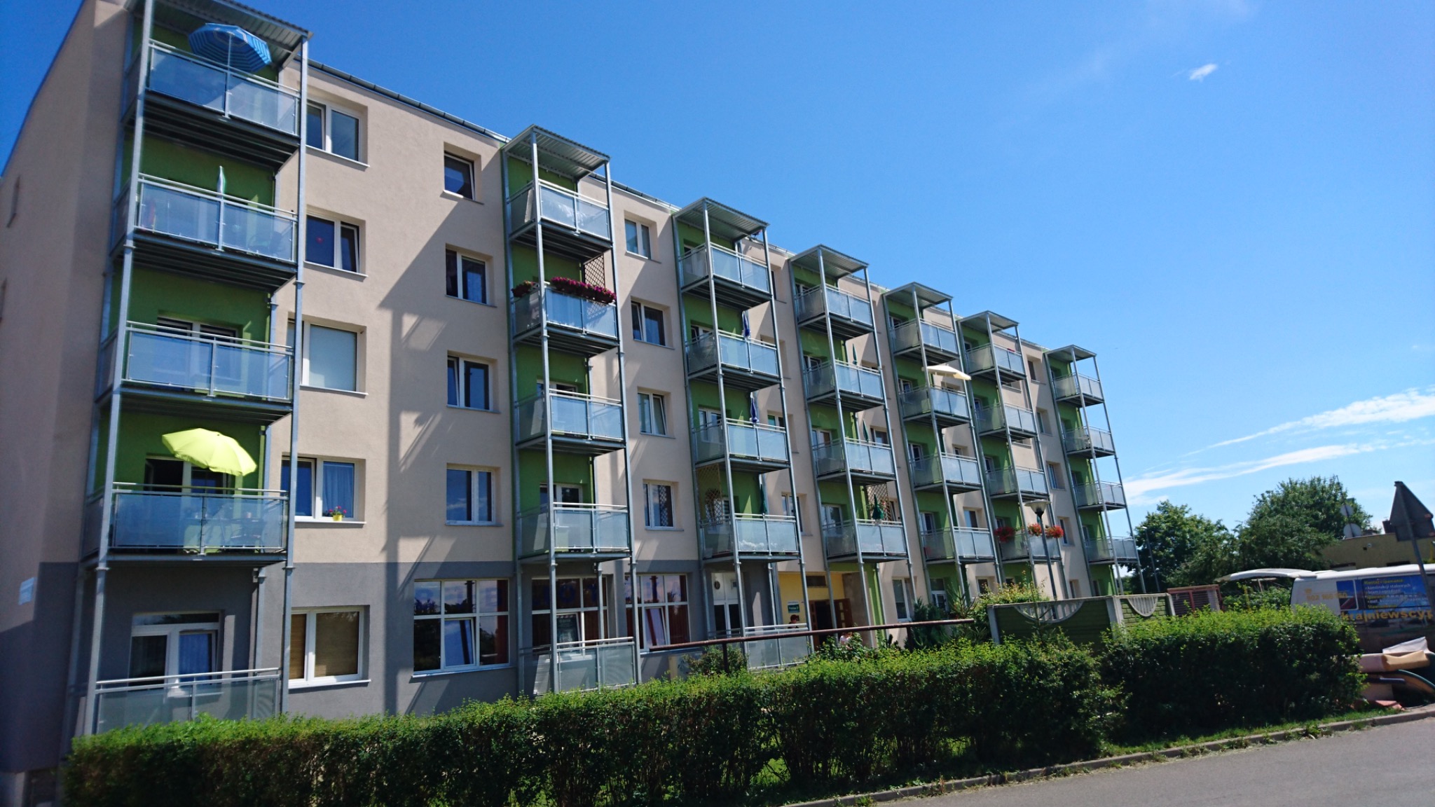 Wielopiętrowy budynek mieszkalny z balkonami o stalowej konstrukcji i szklanych balustradach, widok z dołu w słoneczny dzień.