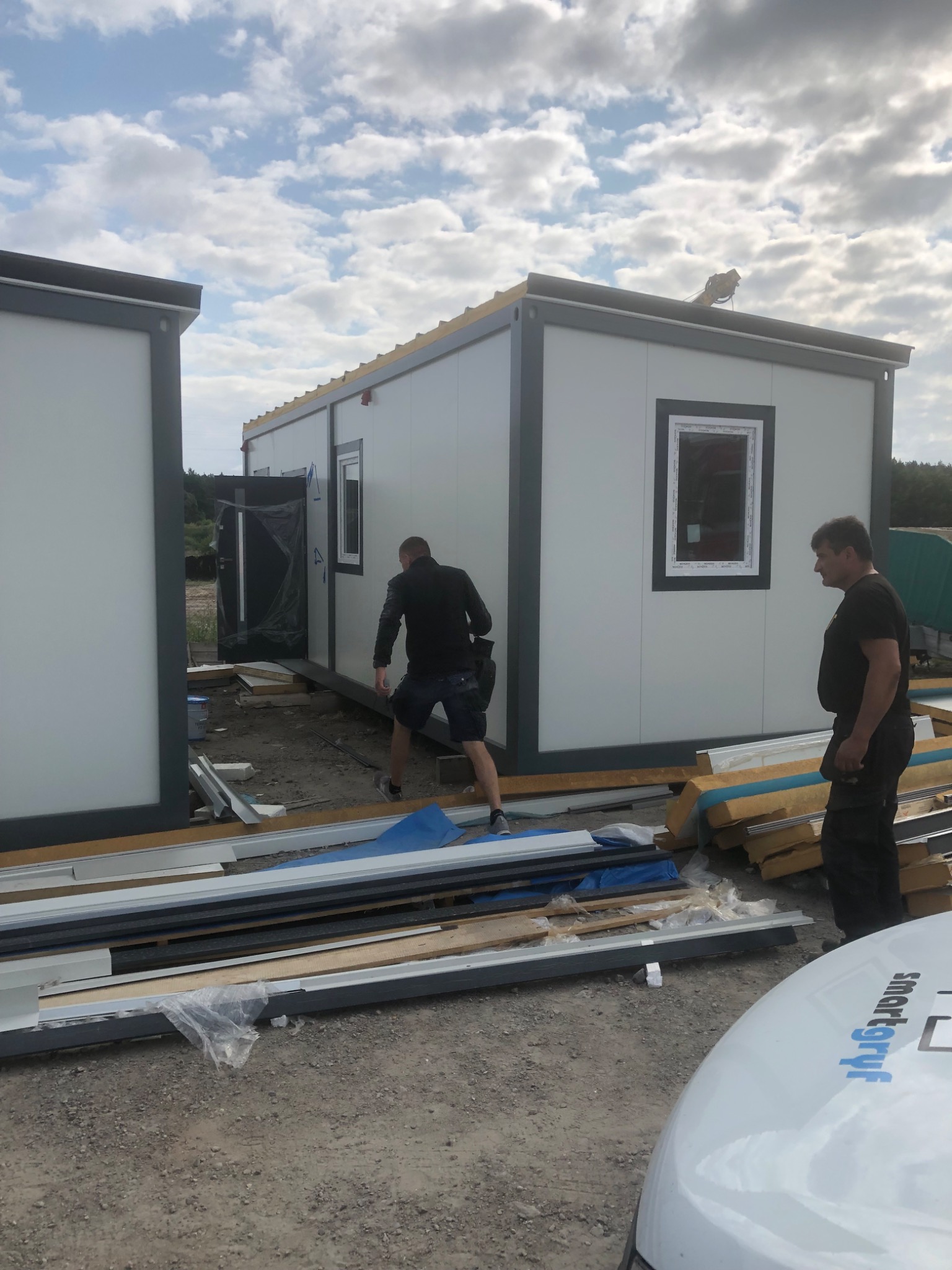 Montaż modułowych kontenerów biurowych na placu budowy; widoczne elementy konstrukcyjne i pracownicy.