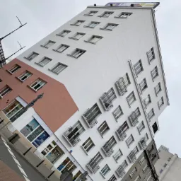 Wysoki budynek z białą elewacją, częściowo pomalowaną na różowo, z reklamą LG na dachu, sfotografowany pod kątem z poziomu ulicy.