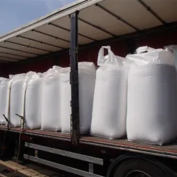 Ciężarówka z naczepą załadowana rzędami dużych, białych worków z nawozem (prawdopodobnie mocznik 46%), zabezpieczonych pasami transportowymi.