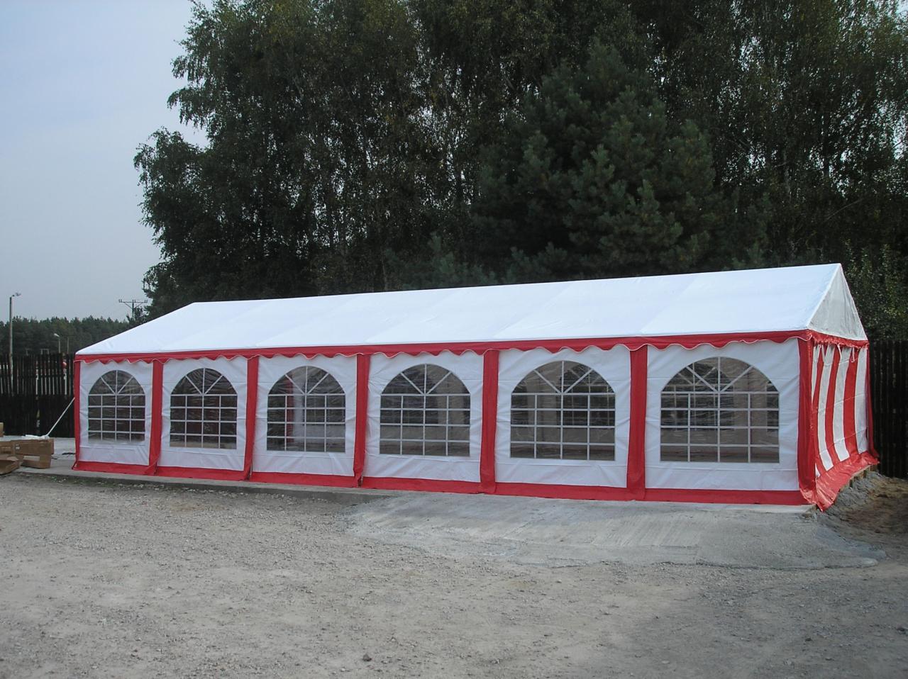 Biały namiot halowy z czerwonymi akcentami, widoczne okna z drobnymi podziałami, teren utwardzony, w tle drzewa.