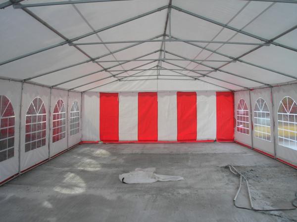 Wnętrze hali namiotowej z metalową konstrukcją, białym dachem i ścianami z czerwono-białymi pasami oraz oknami w kształcie łuków. Na betonowej podłodze leżą resztki folii ochronnej.