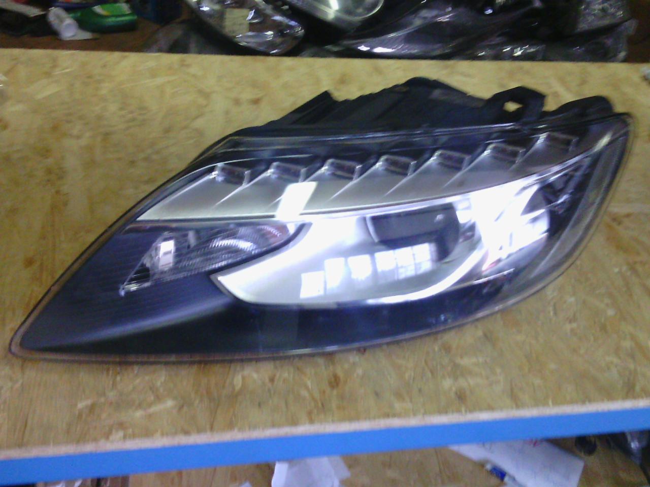 Reflektor samochodowy LED na drewnianym blacie. Nowoczesny design, srebrne akcenty, widoczne mocowania. Element tuningu optycznego pojazdu.