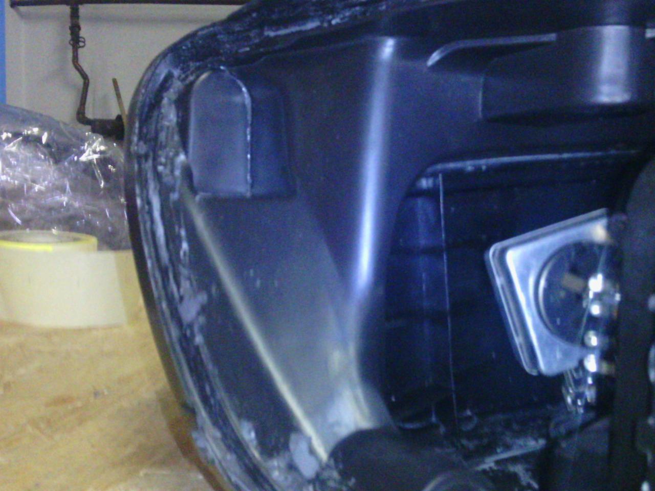 Reflektor samochodowy w trakcie naprawy, widoczne ślady kleju i taśma maskująca. Detal lampy przed montażem w pojeździe.