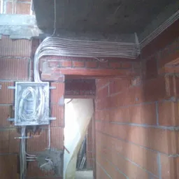 Rozprowadzenie przewodów elektrycznych w ścianie z cegły w trakcie budowy domu w Wieliczce, widoczna puszka instalacyjna i wiązka kabli pod sufitem.