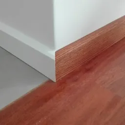 Połączenie dwóch rodzajów podłóg: polerowany beton i ciemne drewno, oddzielone białą listwą przypodłogową i drewnianym cokołem.