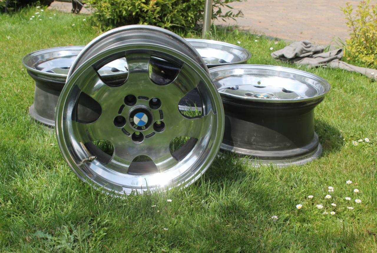 Aluminiowe felgi BMW, po czyszczeniu, leżące na trawie. Widoczne refleksy świetlne i detale polerowania.