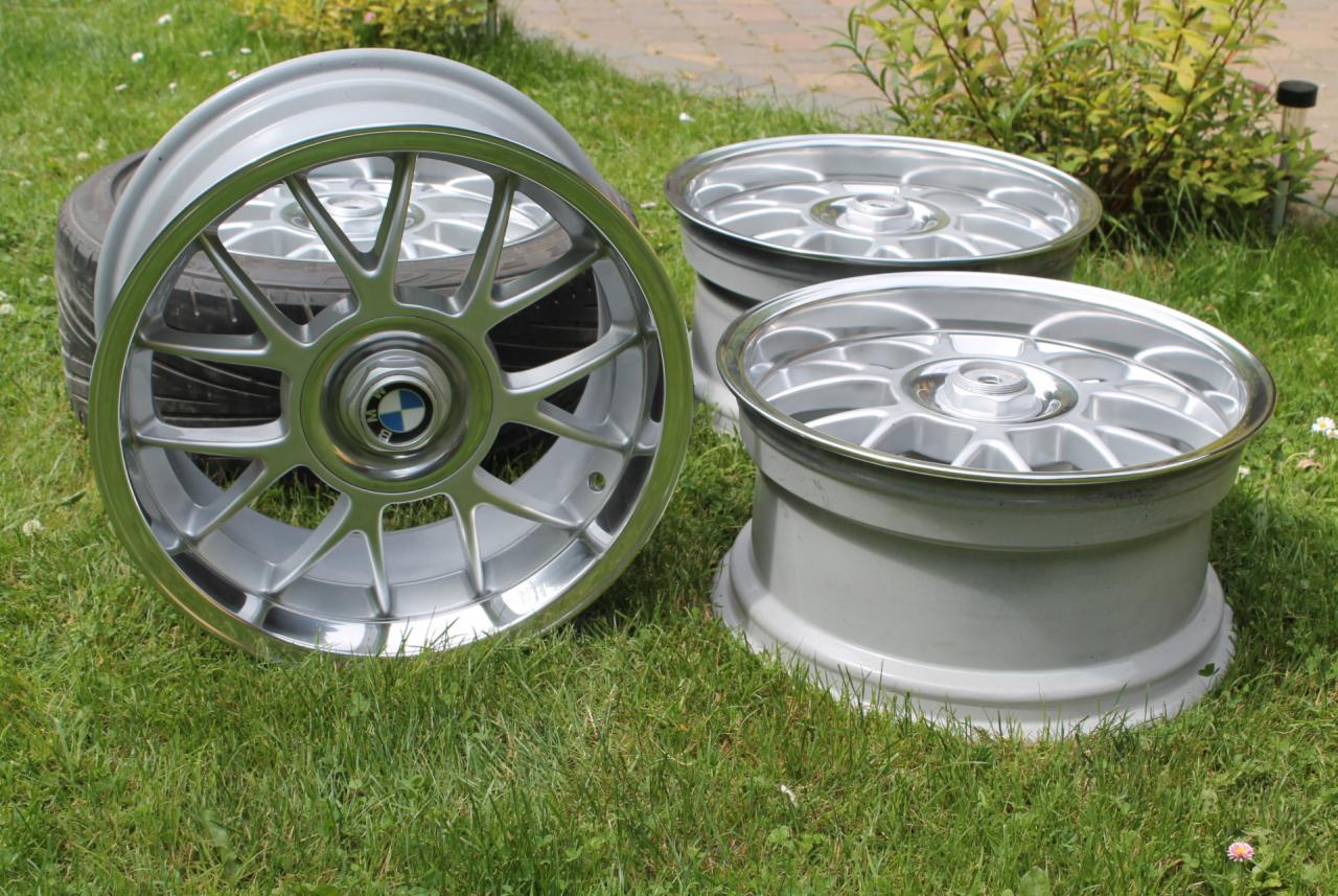 Aluminiowe felgi BMW po renowacji, leżące na trawie. Widoczne trzy felgi, jedna z oponą. Błyszcząca powierzchnia, precyzyjne detale.