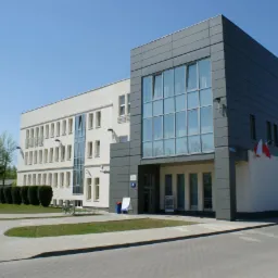 Nowoczesny budynek biurowy w Kozienicach z szarą elewacją i dużymi oknami, widok z zewnątrz na chodnik i trawnik.