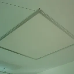 Kwadratowa lampa LED z aluminiową ramą, zawieszona na linkach, oświetla sufit. Minimalistyczny design.