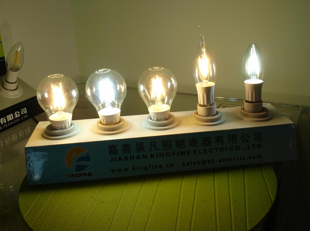 Różne typy żarówek LED na białej listwie z logo Kingfine, prezentacja oferty oświetleniowej. Żarówki w kształcie tradycyjnej żarówki, płomyka i świeczki.