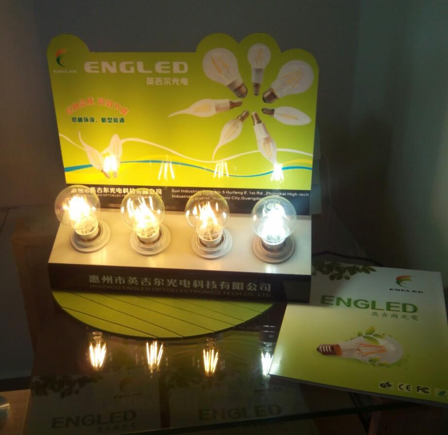 Ekspozycja żarówek LED marki ENGLED na stoisku reklamowym z ulotkami. Cztery żarówki na blacie, z czego jedna wyraźnie jaśniejsza.