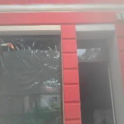 Fragment elewacji budynku z pomalowanymi na czerwono elementami dekoracyjnymi wokół okien i drzwi; okno zabezpieczone folią, widoczna drabina oparta o ścianę.