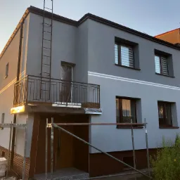 Dom jednorodzinny w Radzionkowie po częściowym nałożeniu szarego tynku, widoczne rusztowania i drabina na elewacji.