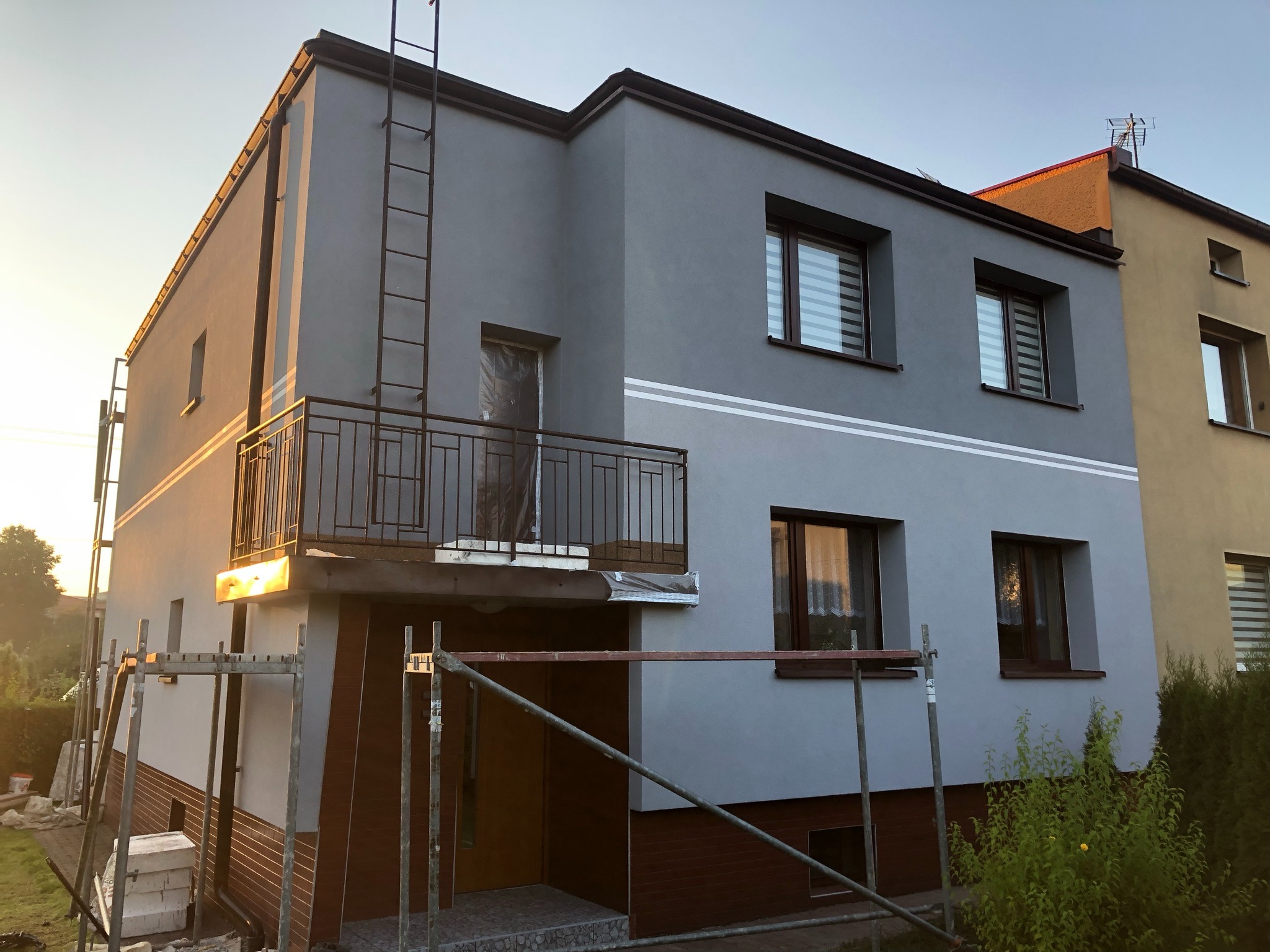 Dom jednorodzinny w Radzionkowie po częściowym nałożeniu szarego tynku, widoczne rusztowania i drabina na elewacji.