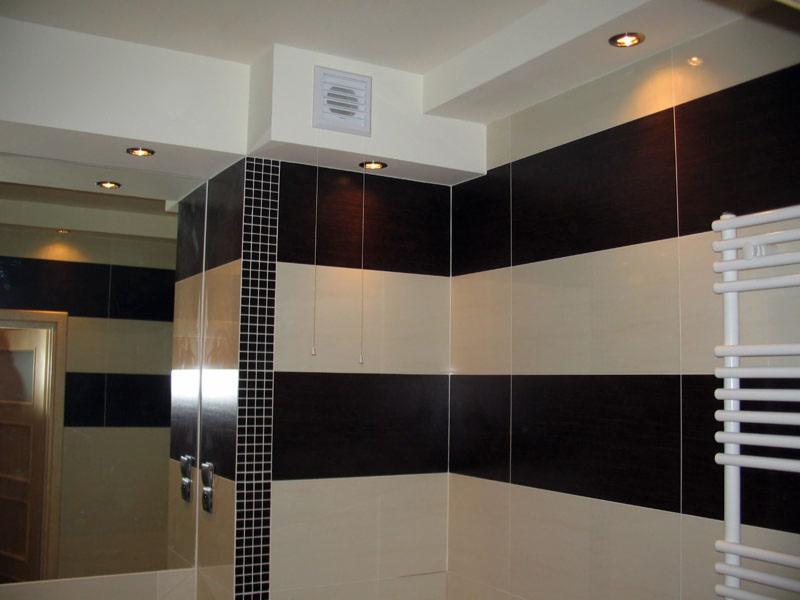 Wykończona łazienka z poziomymi pasami z płytek w kolorze kremowym i ciemnobrązowym, grzejnik drabinkowy i lustro z widocznymi bateriami.