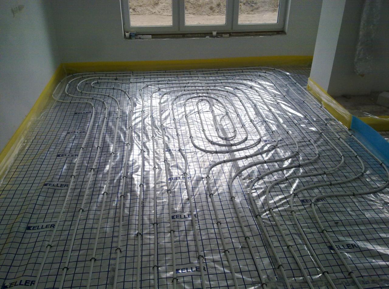 Ułożone rury ogrzewania podłogowego na folii z siatką w jasnym pomieszczeniu, widok z góry. Rury ułożone w pętle, przygotowane do zalania posadzką.