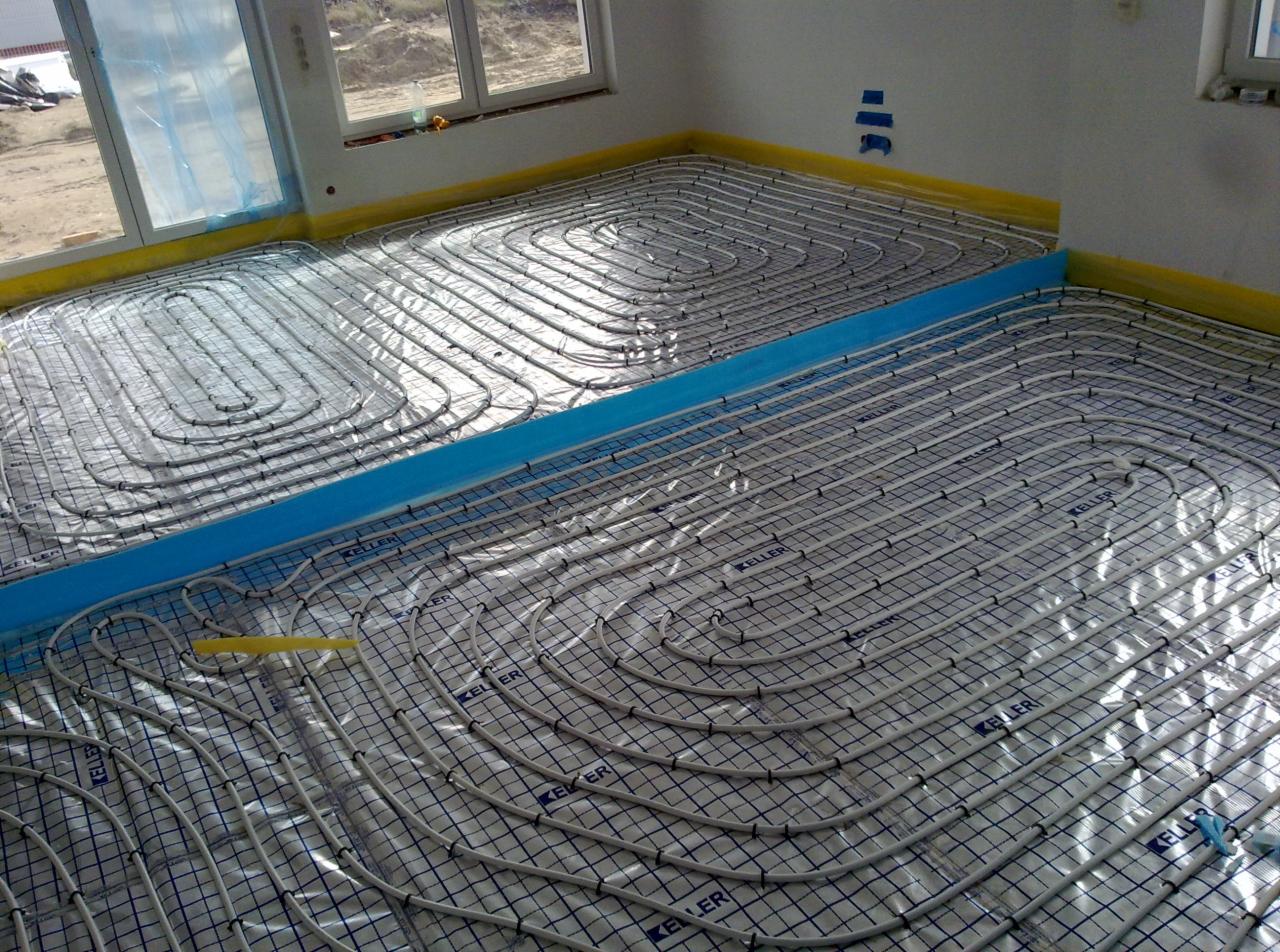 Układanie instalacji ogrzewania podłogowego w nowym budynku, widoczne rury grzewcze na folii z siatką, zabezpieczone ściany folią i taśmą.