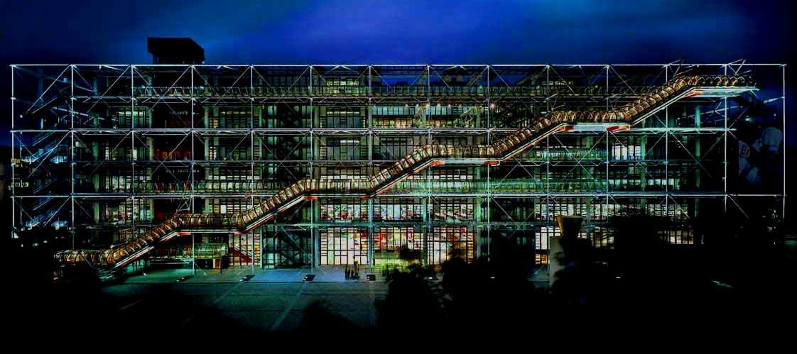 Fasada budynku z zewnętrznymi schodami ruchomymi w metalowej konstrukcji szkieletowej, nocne oświetlenie, widok z dołu.