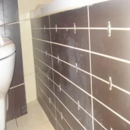 Ciemnobrązowe, poziome płytki z krzyżykami dystansowymi w łazience. Minimalistyczny design z jasnymi fugami i widocznym fragmentem toalety. Ukończone prace glazurnicze.