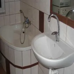 Ukończona łazienka z wanną obudowaną płytkami w beżowo-brązowej tonacji, umywalka z chromowaną baterią i lustro z drewnianą ramą. Widoczna pralka w tle.