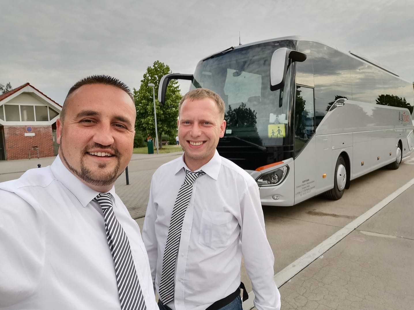 Uśmiechnięci kierowcy w białych koszulach i krawatach na tle srebrnego autobusu z symbolem dzieci. Przewóz osób, komfortowa podróż.