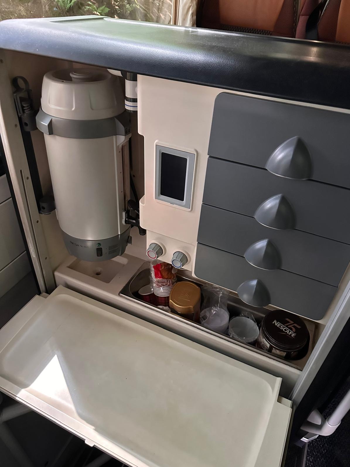 Wnętrze pojazdu z zabudowanym ekspresem do kawy, szufladami i otwartą lodówką. Widoczne akcesoria do kawy, takie jak filiżanki i kawa Nescafe.
